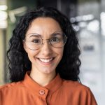 Close-up of a woman with curly hair and glasses, showcasing a big white smile, representing successful dental outcomes at Encinitas Dental Art.