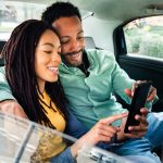 Smiling couple looking at a phone in the back of a taxi, depicting the joy and satisfaction of patients at Encinitas Dental Art.